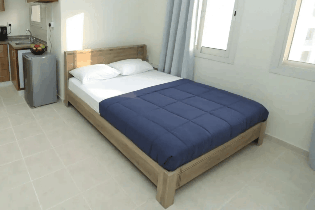 Student accommodation studio room featuring a double bed, compact kitchenette, natural lighting, and modern interior design.